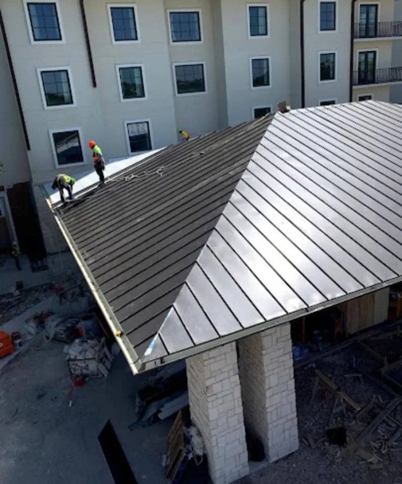 Crew installing standing seam metal roof panels on a commercial project in Garland